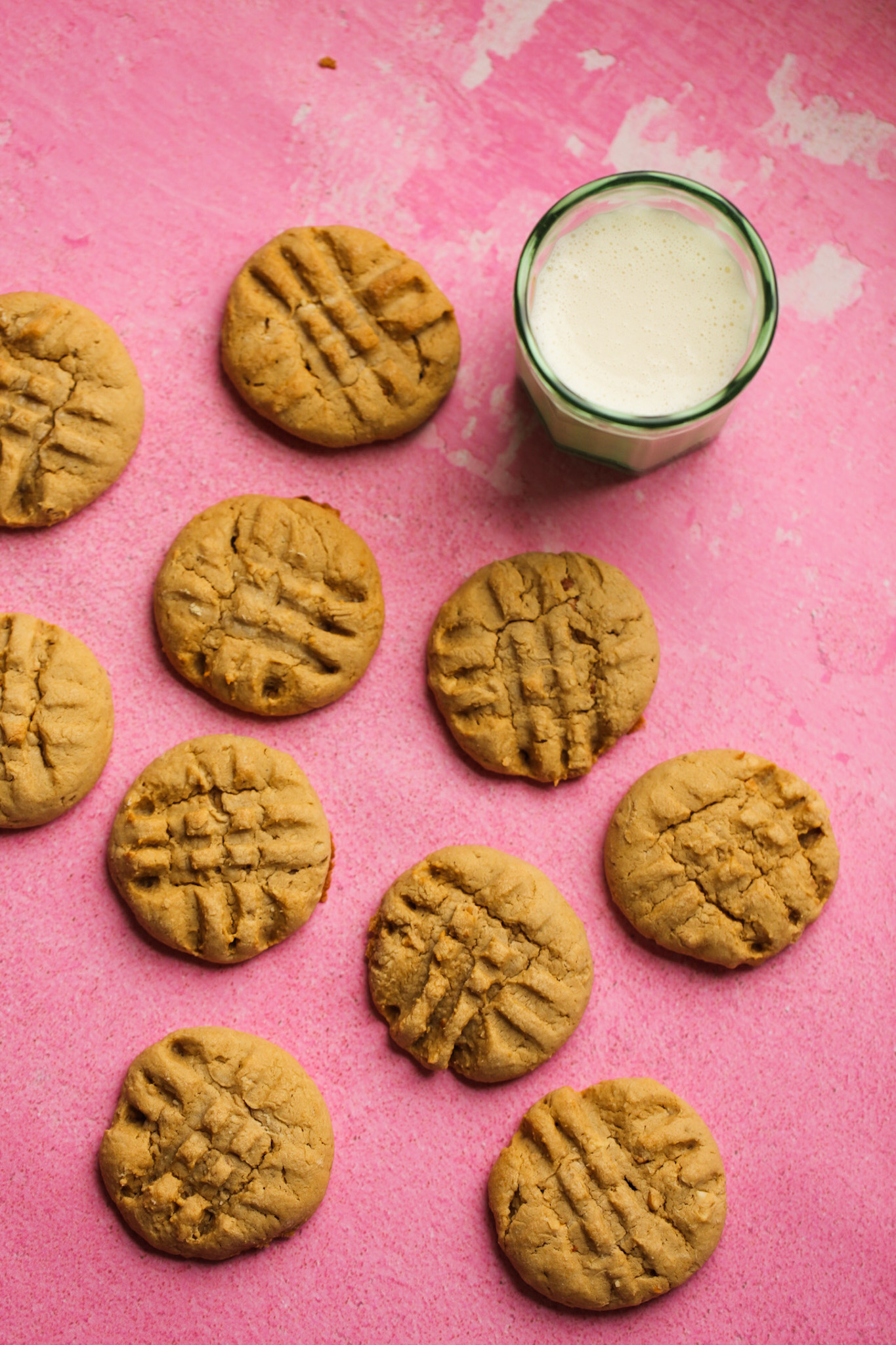 galletas de mantequilla de maní de arce con un vaso de leche de soja sobre una superficie rosa