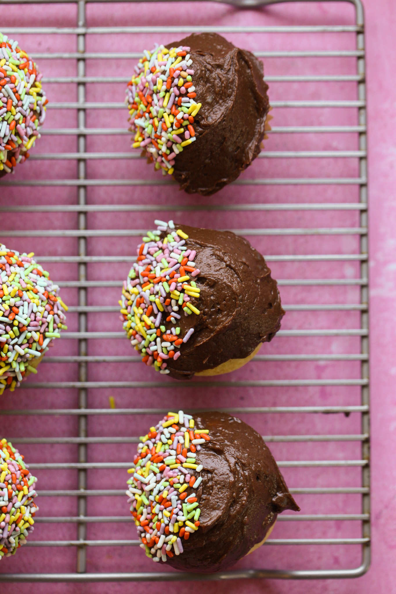 yellow chocolate cupcakes with rainbow sprinkles on cooling rack